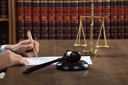 48226466 - cropped image of male judge writing on legal documents at desk in courtroom