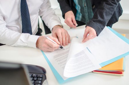 Businessman signing a documents presented by his secretary at the office